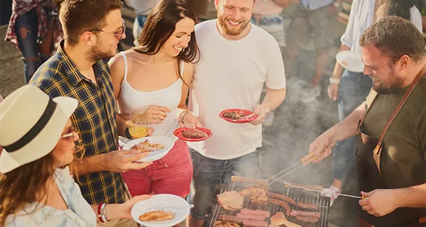 Freunde stehen um einen Grill bei einer Party und unterhalten sich.