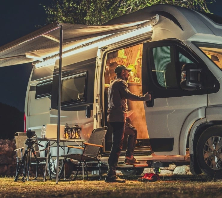 Mann steigt in Wohnbereich eines Campers ein in der Nacht, Markise, Lichterketten