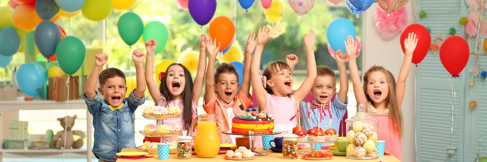 Auf dem Bild sind mehrere Kinder, die sich über die geschmückte Party freuen, vor allem über die Luftballons.