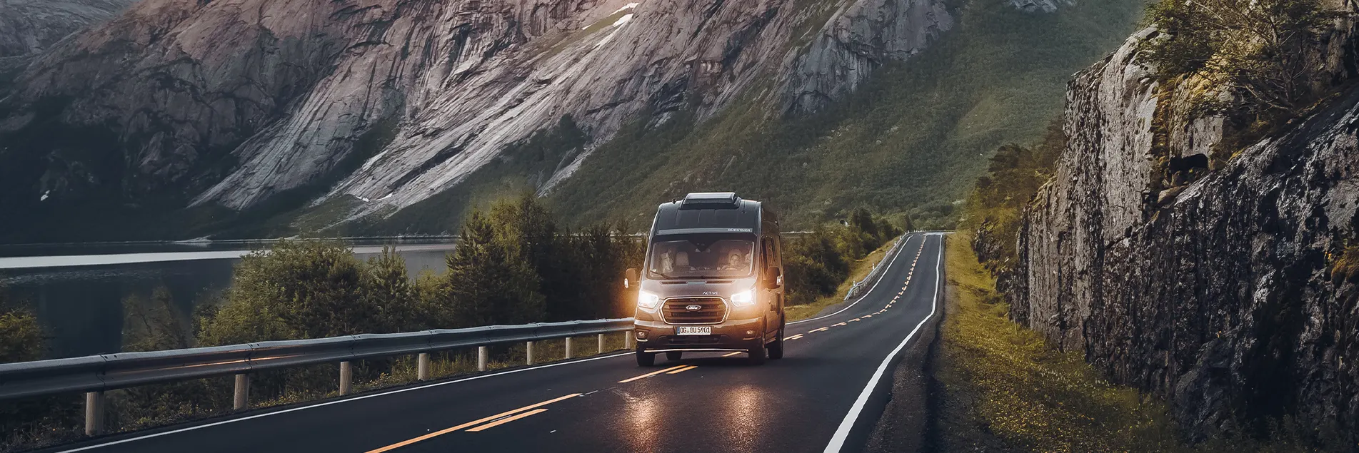 Ein Kastenwagen Caravan fährt über eine Berstraße bei Dämmerung