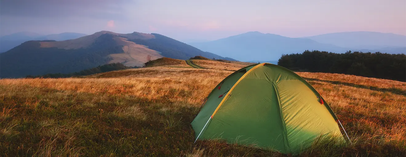 Campingzelt auf einer Tundrawiese vor einem nebelverhangenen Sonnenaufgang